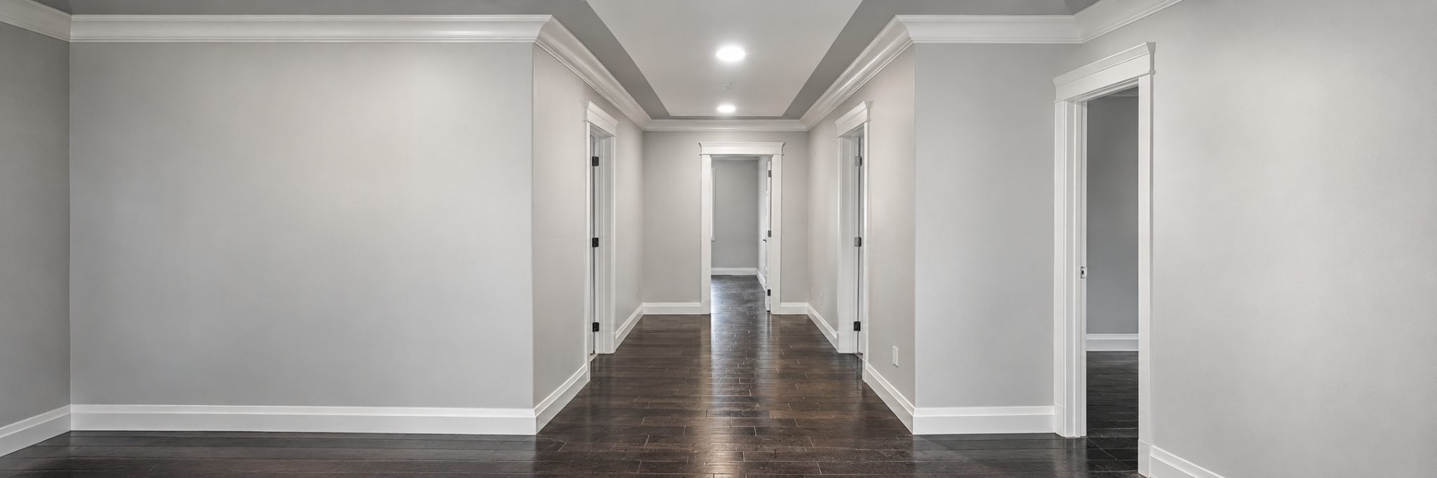 Finished interior hallway with gray walls, white trim, recessed lighting, and dark flooring